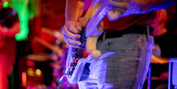 Close-up of musician, lit up with a blue light, playing guitar.